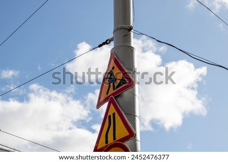 Three signage attached to a pole against a blue sky backdrop with overhead power lines. The cumulus clouds add to the scenic view, showcasing the importance of electrical supply in public utilities