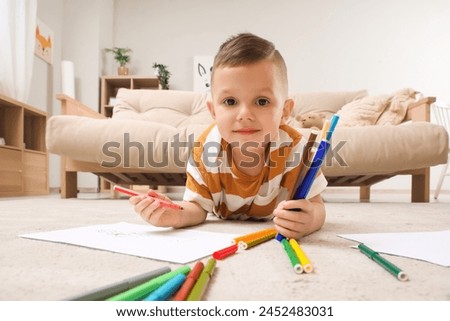 Cute little boy drawing with felt-tip pens on floor at home