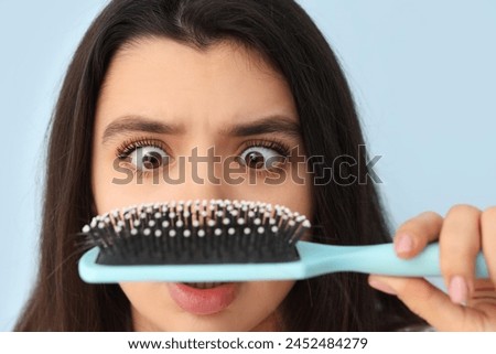 Stressed young woman with hair loss problem and brush on blue background, closeup