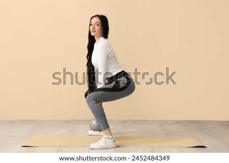 Portrait of sporty young woman exercising with kettlebell on beige background