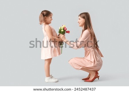 Little girl greeting her mom with Mothers Day with bouquet of tulips on grey background