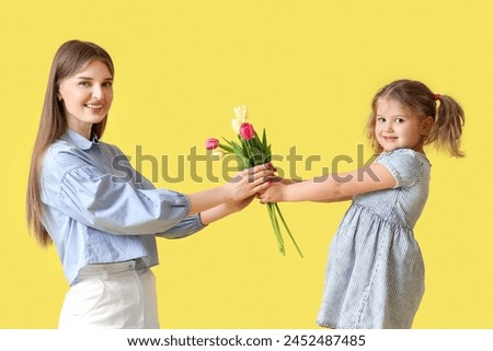 Little girl greeting her mom with Mothers Day with bouquet of tulips on yellow background