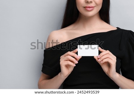 Woman holding blank business card on light grey background, closeup. Space for text