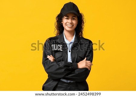 Beautiful young happy African-American policewoman on yellow background Royalty-Free Stock Photo #2452498399