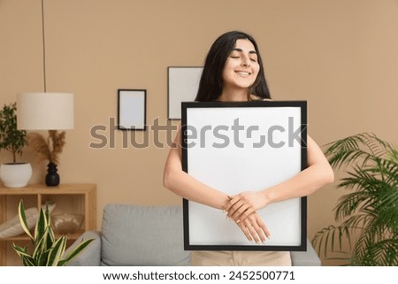 Young woman with blank picture frame in living room