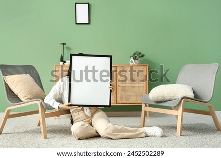 Young woman sitting with blank picture frame near armchairs in living room