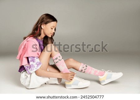 A stylish teenage girl in vibrant attire sits cross-legged on the ground exuding calmness and poise. Royalty-Free Stock Photo #2452504777