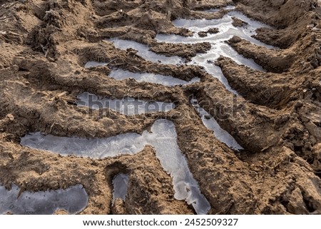 a deep track from a heavy car in a field, a plowed field with frozen ground and traces of agricultural machinery