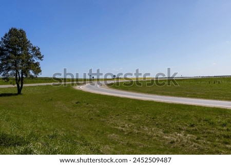an asphalt highway turning right, a tree growing on the side of the highway Royalty-Free Stock Photo #2452509487