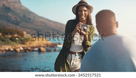 Happy couple, photography and laughing with camera by beach for funny memory or outdoor moment in nature. Woman or photographer taking picture of man with smile for adventure or tour by ocean coast