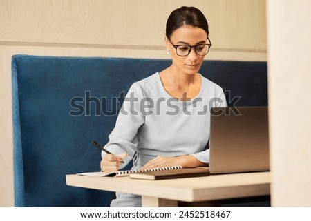 Secretary, laptop or businesswoman with notebook or schedule for daily routine, checklist ideas. Agenda, organise or receptionist writing to do list in cafe with notepad, page or book for planning Royalty-Free Stock Photo #2452518467