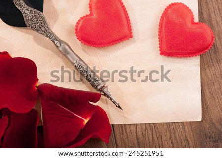 Love letter. Closeup image of vintage paper with copy space and feather pen arranged on wooden table and decorated with rose petals and hearts