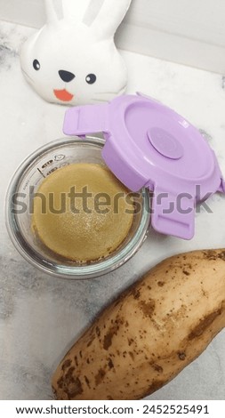 A puree food for baby in the complementary food phase with a soft and mushy texture in glass bowl and next to a white rabbit doll.