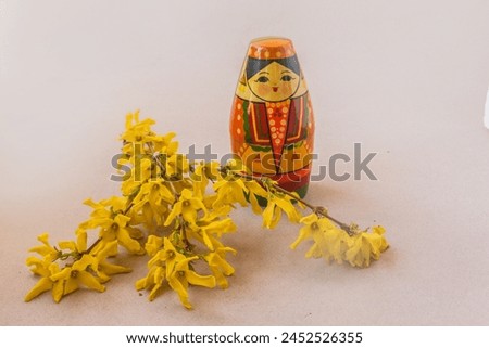 Wooden toy souvenir stylized as a Tatar girl next to flowering branches of forsythia  on a gray background. Mass production. Navruz holiday concept.