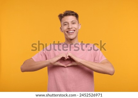 Happy man showing heart gesture with hands on orange background