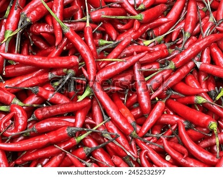 a photography of a pile of red hot peppers with green stems.