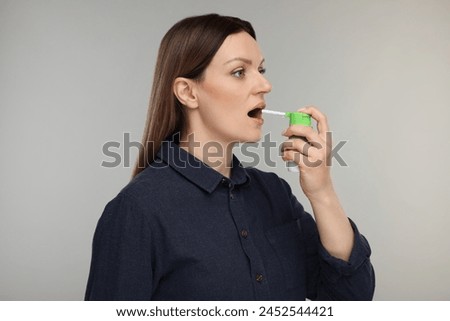 Woman using throat spray on grey background Royalty-Free Stock Photo #2452544421
