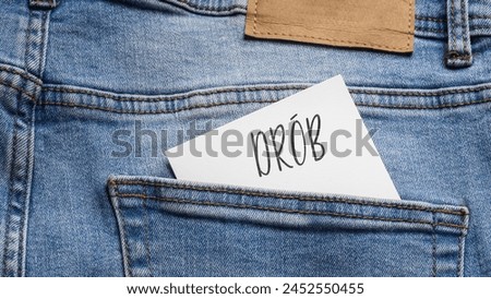 White card with a handwritten inscription "Drób", inserted into the pocket of blue pants jeasnow (selective focus), translation: Poultry