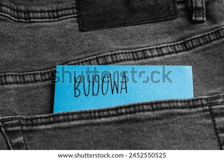 Blue card with a handwritten inscription "Budowa", inserted into the pocket of gray pants jeasnow (selective focus), translation: Construction