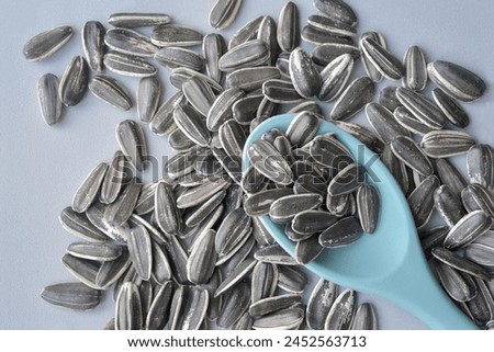 Close up photograph of roasted sunflower seeds in shell and a spoon of light blue colour Top view