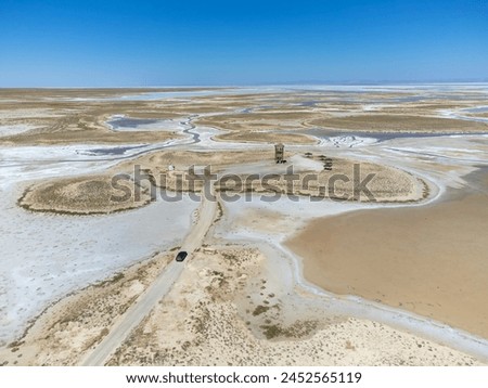 Drone view of car moving along road on dead salt lake Tuz in Turkey. Landscape is like on Moon or Mars, everything dried covered with salt. Here edible salt mined and processed in factory or factory. Royalty-Free Stock Photo #2452565119