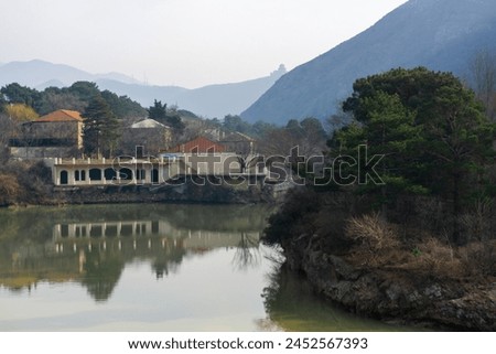 View of the Mtkvari (Kura) river from the bridge in the city of Mtskheta. High mountain and Jvari monastery on the hill. Reflection of the sky, buildings and trees in the water. Royalty-Free Stock Photo #2452567393