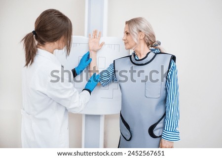 A woman doctor takes a picture of a woman patient’s hand against the background of a special target to make an x-ray in an office with an x-ray machine, medical equipment.
