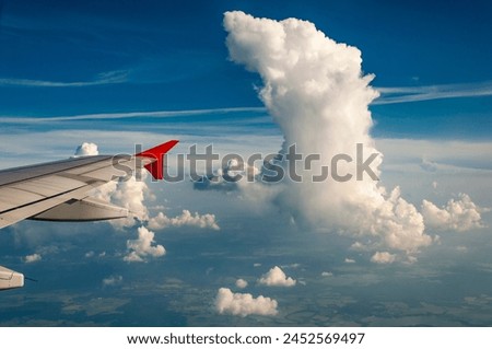 View from the window of a passenger airplane at high altitude with a rising cloud in the atmosphere on the horizon and a blue sky