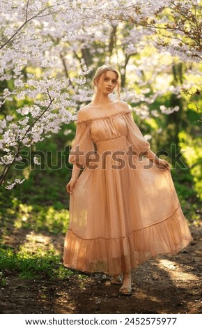 Pretty young blonde girl with  in vintage pink dress standing in spring park near pink blossom flowers. Tenderness romantic  model posing with emotions.