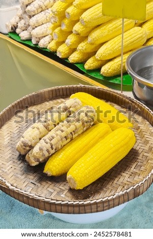 Steamed and grilled corn cobs presented on a woven basket, drizzled with butter, capture the essence of street food with their vibrant, tempting colors and rustic charm. Vertical format Royalty-Free Stock Photo #2452578481