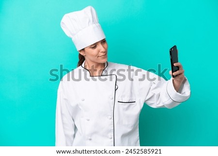 Young caucasian chef woman isolated on blue background making a selfie