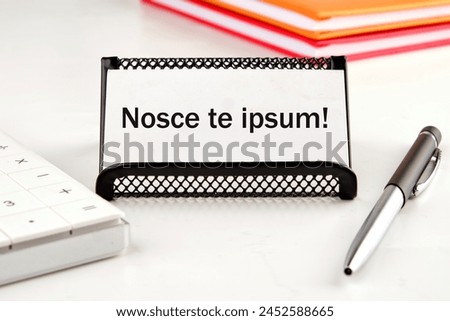 Latin proverb NOSCE TE IPSUM (know yourself) on a white business card next to a calculator, notepad and pen