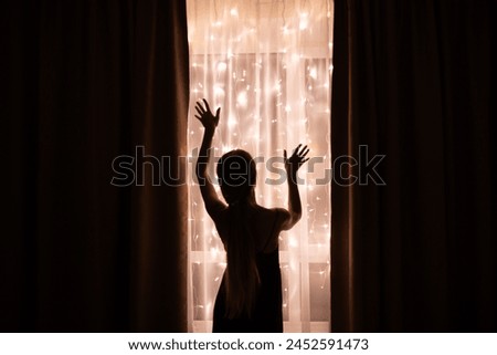 Dark silhouette of a woman standing near window with Christmas illumination.