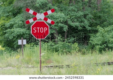 Stop sign and Saint Andrew s cross - railway crossing in the forest. A forest railway line among lush trees on a July afternoon. Road signs at a railway crossing. 