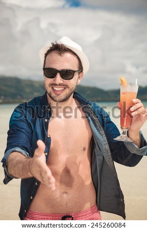 Happy young man getting ready for handshake while holding a orange cocktail in his left hand, seaside picture.