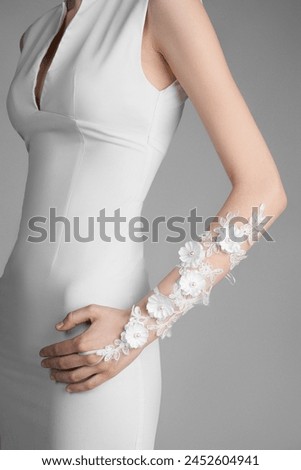 Cropped close-up shot of a girl in a white dress with a white long fingerless gloves decorated with flowers. A girl in the white openwork mittens is posing on a pastel background. Side view. Royalty-Free Stock Photo #2452604941