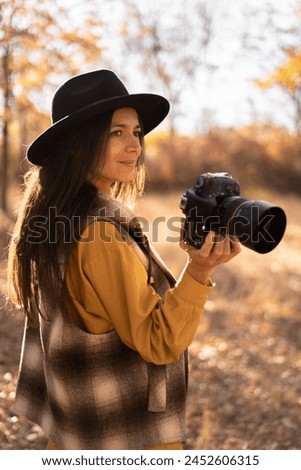 Hispanic woman is a professional photographer in black hat with dslr camera, outdoor in autumn forest, Portrait.