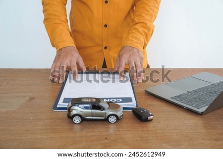People signing car documents or rental papers Writing your signature on a contract or agreement Buying or selling a new or used vehicle The car keys are on the table.