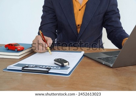 People signing car documents or rental papers Writing your signature on a contract or agreement Buying or selling a new or used vehicle The car keys are on the table.