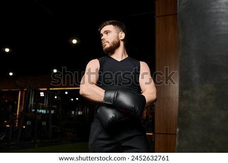 Handsome man with a beard wearing boxing gloves, throwing powerful punches at a punching bag in a gym. Royalty-Free Stock Photo #2452632761
