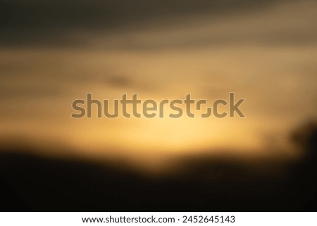 A blurry photo of a sunset with a hazy background. Scene is serene and peaceful, as the sun sets over the horizon