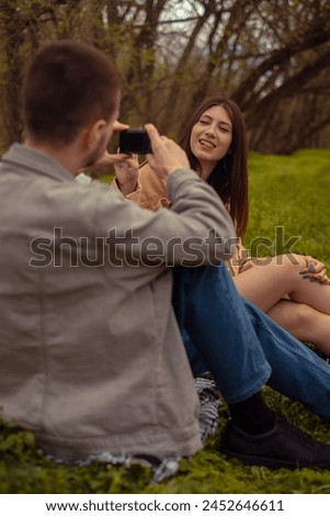 A man takes a photo of his girlfriend on his phone. A young couple camping in the forest, enjoying active outdoor leisure and travel adventures.