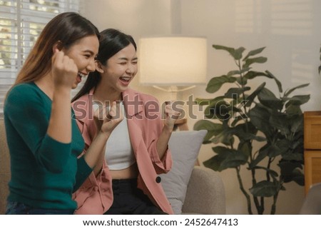Two beautiful Asian teenage girls are having fun watching entertainment together at home on the sofa, Two beautiful female friends spend a weekend together in ultimate bliss in an apartment.