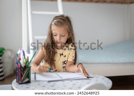 Cute little girl enjoys painting. Girl drawing and coloring picture with color pencil in her room at home
