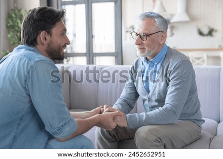 Young adult caucasian son listening and supporting his old elderly senior father at home indoors. Happy father`s day! Care and love concept. I love you, dad!