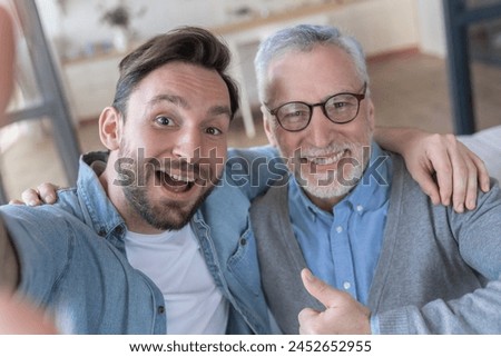 Cheerful caucasian adult son and old senior father taking making selfie at home, spending time together. Fatherhood. Happy father`s day! I love you, dad!