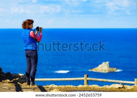 Woman with camera take travel picture from sea landscape, Atlantic ocean and Asturias coast at Cape Penas in north Spain.