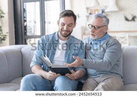 Young loving adult son discussing a novel, new book he read with his elderly old senior father. Family time, togetherness. Happy father`s day! I love you, dad!