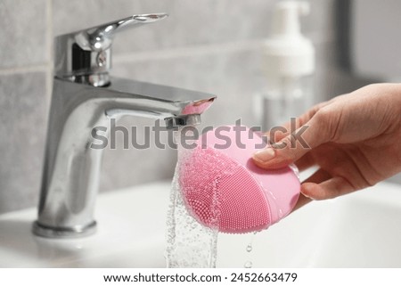 Young woman washing facial brush in bathroom, closeup