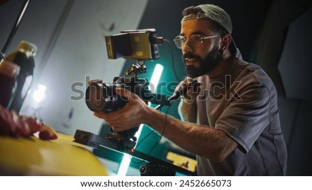 Focused Male Cinematographer With Beard And Glasses Operates Professional Camera On Film Set, Capturing Dynamic Shots Under Vibrant Studio Lights, Showcasing Videography Techniques And Equipment.